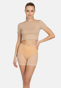 Beige crop top, amelyet bőrszínű, magas derekú kompressziós sorttal párosítottak. Az anyag sima, és áttetsző részletek találhatók a comboknál. Egyszerű és varrás nélküli kialakítás.