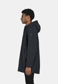 Giacca con cappuccio blu navy dal design elegante, tasca laterale con zip e tessuto testurizzato. Presenta una toppa con logo sulla parte superiore del braccio.