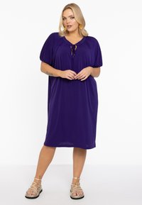 Lila knielanges Kleid mit kurzen Puffärmeln, rundem Ausschnitt und einem Bindeband vorne. Glatte Stoffoberfläche.