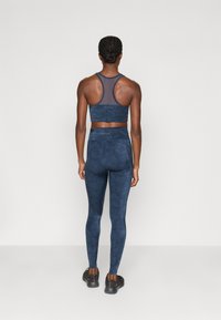 Set sportiv de culoare albastru marin, format dintr-un sutien scurt și colanți cu talie înaltă, având un model texturat. Materialul este ajustat și elastic.