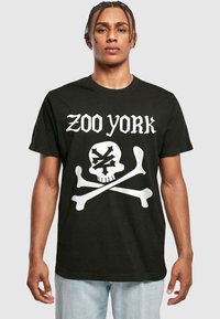 Juodas medvilnės marškinėliai su balta kaukolės ir kaulų grafika, virš kurios yra užrašas "ZOO YORK". Trumpomis rankovėmis, laisvas siluetas, apvalia iškirpte.
