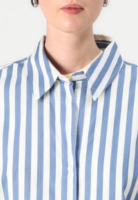 Blue and white striped collared shirt with a button front, featuring a soft texture and evenly spaced vertical stripes.