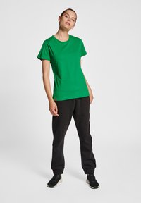 Grön bomullströja med korta ärmar och rundad halsringning, matchad med svarta joggers och svarta träningsskor.