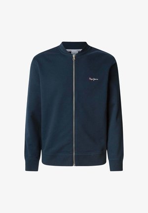 Tamsiai mėlyna užtrauktuku užsegama striukė, pagaminta iš minkštos medžiagos, su gipiūriniais apykakle ir rankogaliais, ant kairiojo krūtinės puikuojasi mažas raudonas logotipas.