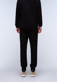 Zwarte sweatshirt en broek set, gemaakt van een katoenmix. Eenvoudig ontwerp met ribbelboorden en een taps toelopende pasvorm. Beigekleurige sneakers met zwarte accenten.