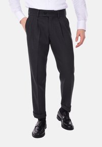 Pantaloni grigio carbone con pieghe, vita regolabile e una texture del tessuto liscia, abbinati a mocassini neri.