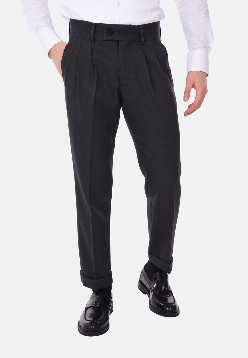 Pantaloni grigio carbone con pieghe, vita regolabile e una texture del tessuto liscia, abbinati a mocassini neri.