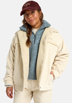 Romiggekleurige corduroyjas met fleece voering, gelaagd over een zachte blauwe fleece pullover. Accessoires zijn onder andere een kastanjebruine corduroy pet.