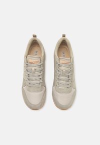 Béžové tenisky s vrchní částí ze síťoviny a semiše, šněrovací design, texturovaná podešev a malý poutko na patě. Obsahuje štítek "SKECHERS".