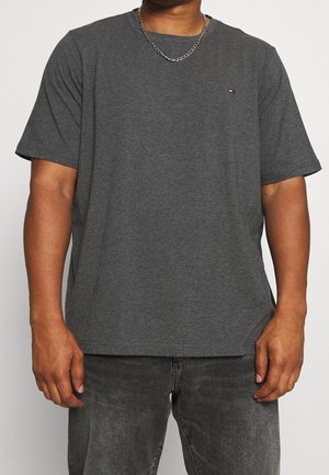 Homme portant un t-shirt à manches courtes gris foncé et un jean noir délavé, avec une chaîne en argent visible autour du cou.