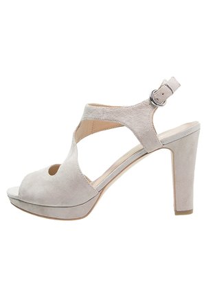 Beżowe sandały na wysokim obcasie z zamszu, z odkrytymi palcami, paskiem wokół kostki, krzyżowym zdobieniem i masywnym obcasem zapewniającym stabilność.