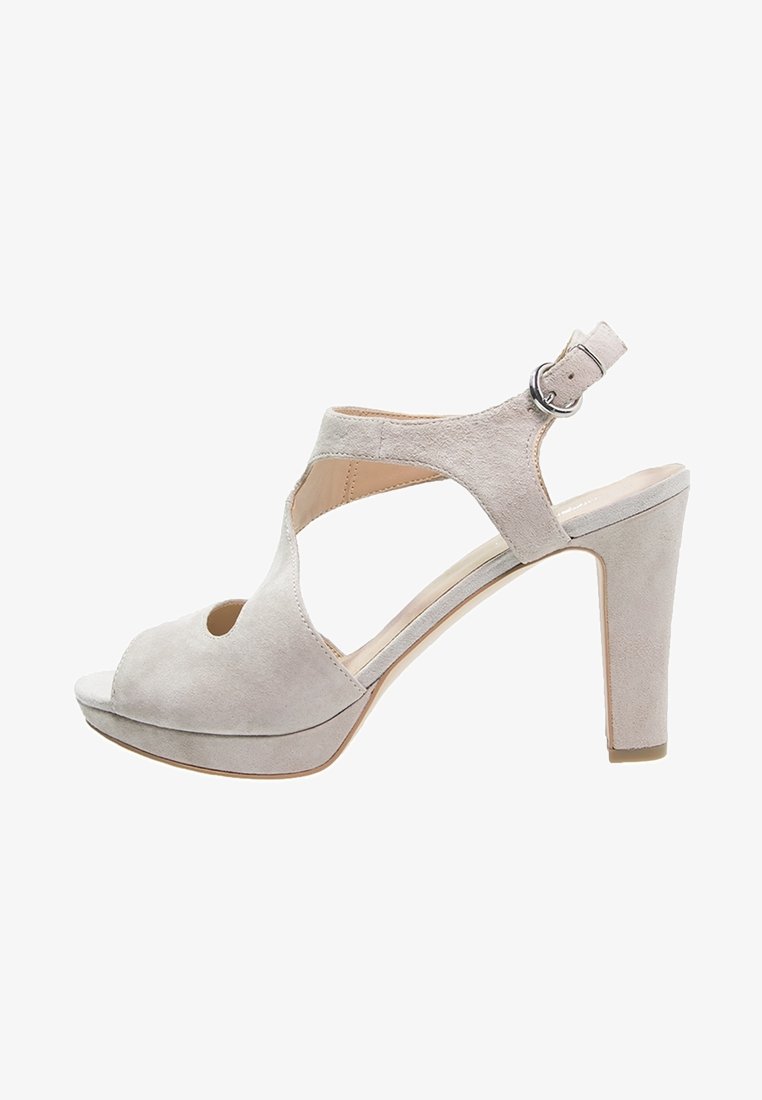 Sandales à talons hauts en daim beige avec bout ouvert, bride à la cheville, design croisé et talon épais pour plus de stabilité.