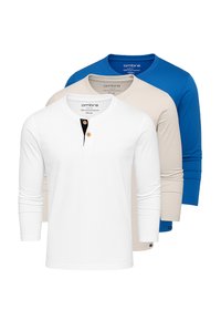 Tre långärmade skjortor: vit, beige och blå. Har rundad halsringning och framträdande knappdetalj på den vita skjortan. Slät tygtextur.