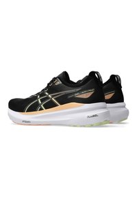 Zwarte sportieve schoenen van mesh-stof, ontworpen met oranje en groene accenten, met een dikke witte tussenzool en een gestructureerde rubberen loopzool.