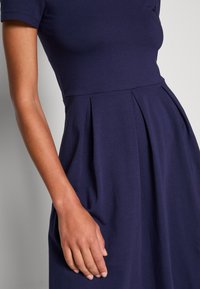 Abito blu navy realizzato in tessuto morbido, con maniche corte, corpetto aderente e gonna plissettata con una texture liscia.