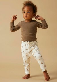 Haut marron à manches longues associé à un pantalon crème orné d'un imprimé girafe. Le pantalon possède une fermeture avec cordon de serrage et des boutons latéraux.