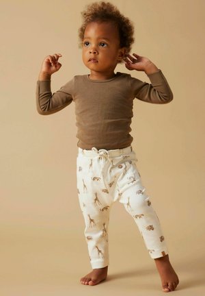 Haut marron à manches longues associé à un pantalon crème orné d'un imprimé girafe. Le pantalon possède une fermeture avec cordon de serrage et des boutons latéraux.