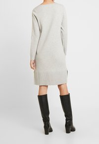 Abito grigio a maglia con maniche lunghe, orlo a costine e spacchi laterali, abbinato a stivali in pelle nera al ginocchio. Tessuto liscio, vestibilità rilassata.