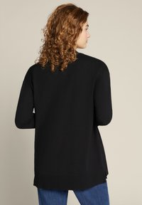 Maglione nero a maniche lunghe con vestibilità comoda, caratterizzato da un collo rotondo e spacchi laterali in fondo. Tessuto morbido e design semplice.