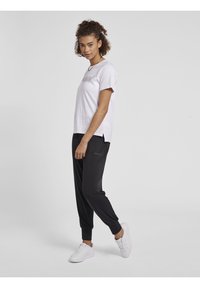 Hvid t-shirt med korte ærmer og tekst, parret med sorte tapered joggers. Outfitten har en afslappet pasform og er afsluttet med hvide sneakers.