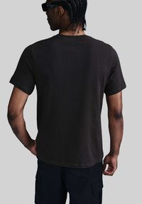 Camiseta de algodón negra de manga corta, cuello redondo y corte relajado, mostrada desde atrás. La tela tiene una textura suave.