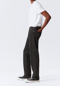 Jeans in denim nero con taglio a gamba dritta, cinque tasche e una sottile texture sfumata. Indossati con una maglietta bianca e sneaker nere.