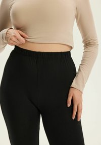 Schwarze Stretchleggings mit einem elastischen Bund, kombiniert mit einem beigen Langarmoberteil. Der Stoff hat eine glatte Textur und ein figurbetontes Design.