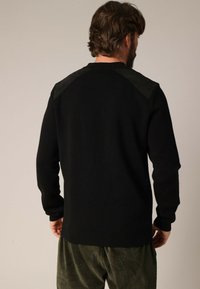 Zwarte gebreide trui met textuuraccenten in zwart op de schouders, lange mouwen en een ronde hals, weergegeven vanuit de achterkant.