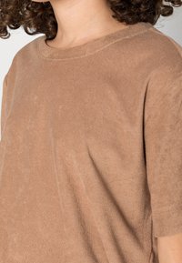 T-shirt en coton marron avec un design décontracté, des manches courtes et un col rond côtelé, offrant une texture douce et un brillant subtil.