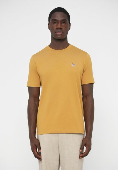 Horčicovo žlté tričko s krátkym rukávom z hladkej látky, s malým vyšitým motívom na ľavej strane hrude. Jednoduchý okrúhly výstrih.