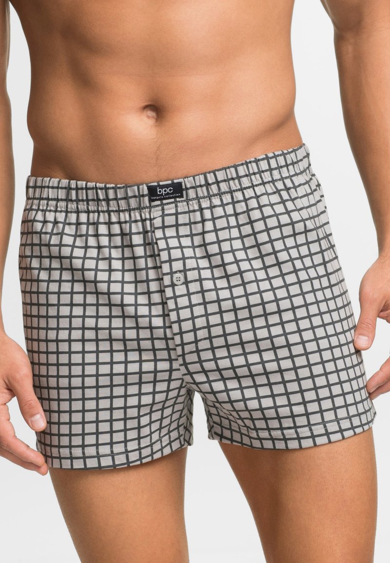 Boxer grigi con un motivo a griglia nera, dotati di un elastico in vita, chiusura con bottone e una texture morbida e liscia. Etichetta del marchio visibile.