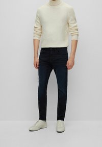 Cream turtleneck sweater, ribbed texture; dark blue jeans, slim fit; light-colored sneakers with minimal detail, flat soles.