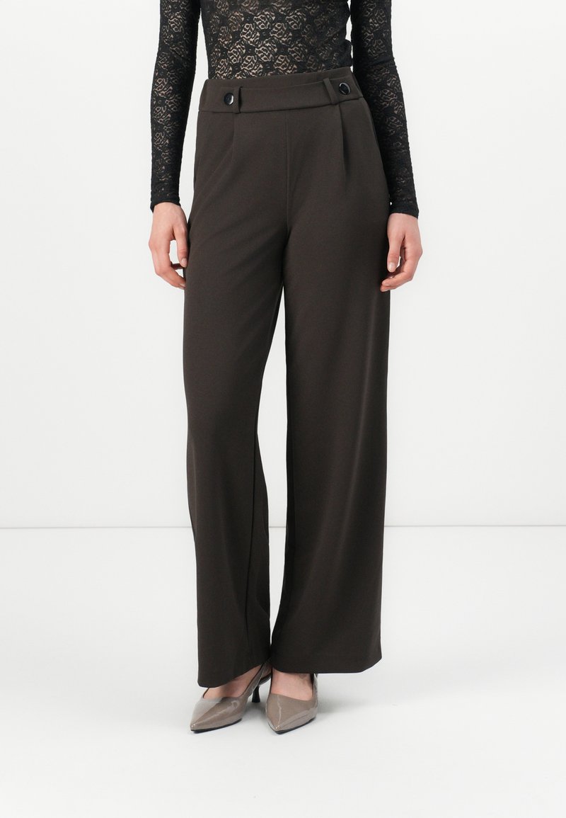 Pantalons larges marron en tissu lisse avec taille haute, présentant deux boutons à l'avant et des plis pour une touche supplémentaire.