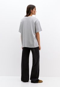 T-shirt en coton gris à manches courtes, coupe décontractée et encolure arrondie, associé à un pantalon large noir et des chaussures marron.
