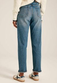 Svijetloplave traperice ravnog kroja, sa pet džepova, vidljivim šavovima i zavrnutim rubovima, u kombinaciji s bijelim tenisicama s plavim prugama.