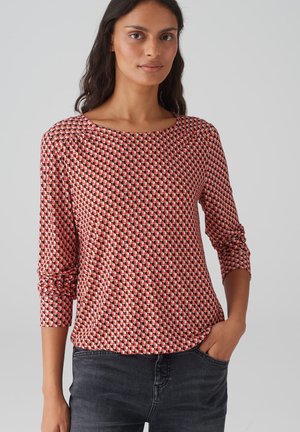 Chemise à manches longues à motifs rouges et noirs avec un col rond et une coupe décontractée, fabriquée en tissu doux, portée avec un jean sombre.