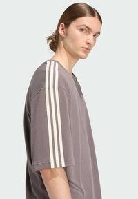 Sivá tričko s krátkymi rukávmi, ktoré má biele zvislé pruhy na ramenách a okrúhly výstrih, vyrobené z mäkkej, textúrovanej bavlnenej látky.