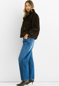 Brown faux fur jacket with a high collar, paired with blue straight-leg jeans and pointed black snakeskin heels. Simple, textured design.