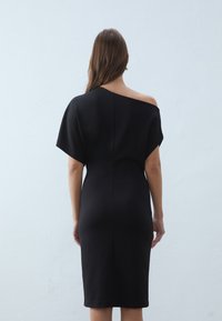 Zwarte off-shoulder jurk met korte mouwen, aansluitende pasvorm en een zoom tot op de knie. Gladde textuur zonder zichtbare patronen of versieringen.