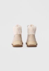 Lys beige ankelstøvler med en blød cremefarvet pelskrave, gummisål og et glat overmateriale. Har en sidelukning for nem adgang.
