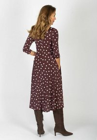Brązowa sukienka w kropki, wykonana z elastycznego materiału, z dopasowanym gorsetem, rękawami 3/4 oraz pełną spódnicą. Brązowe buty za kolano.