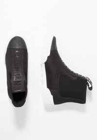 Černé slip-on tenisky s síťovaným svrškem, gumovou špičkou a bílou gumovou podrážkou. Ozdobené logem na přední straně.