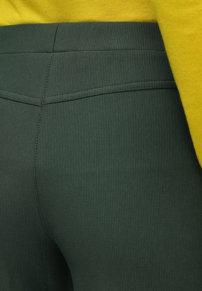 Groene geribbelde broek met een hoge taille en eenvoudige achterzakken, gecombineerd met een geel topje, met een gestructureerde stof en een gladde afwerking.
