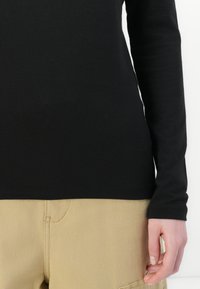 Zwarte langemouwen top van een zachte, gladde stof, met een nauwsluitend ontwerp. Gecombineerd met beige cargo pants met zijzakken.