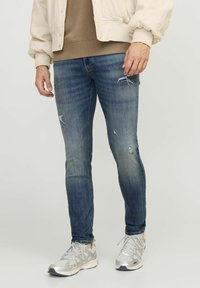 Jeans ajustados de mezclilla azul con detalles desgastados, que presentan una textura suave y un ligero desvanecimiento, combinados con zapatillas deportivas gris claro.