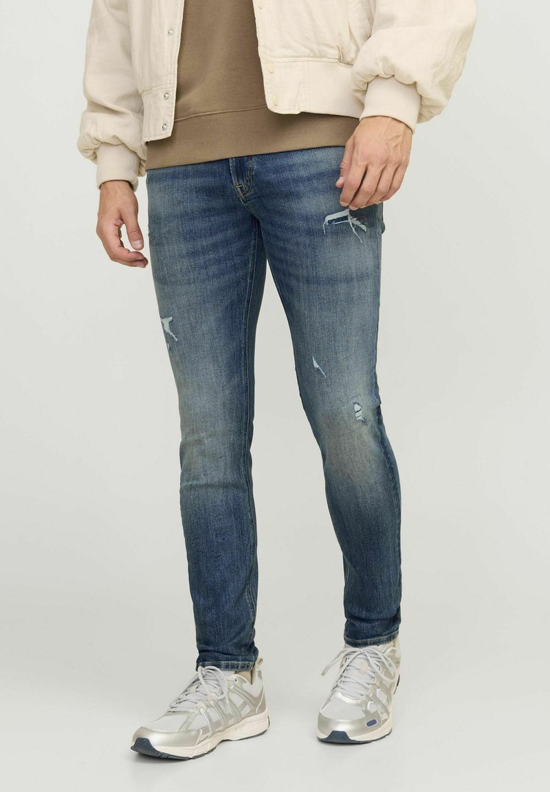 Jeans ajustados de mezclilla azul con detalles desgastados, que presentan una textura suave y un ligero desvanecimiento, combinados con zapatillas deportivas gris claro.