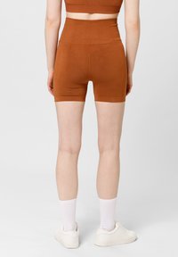 Bruine hoge taille shorts met een gladde textuur, een slim fit ontwerp en een lengte tot halverwege de dijen, gecombineerd met witte sokken en sneakers.