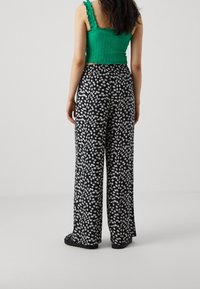 Czarne spodnie w szerokim kroju z białym wzorem kwiatowym, zestawione z zielonym topem w fasonie crop z marszczeniem i falbankowymi ramiączkami, widziane od tyłu.