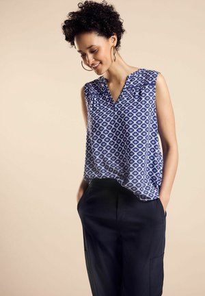 Sleeveless blue blouse with a geometric pattern, featuring a V-neck and relaxed fit, paired with dark cargo pants. Textured fabric.