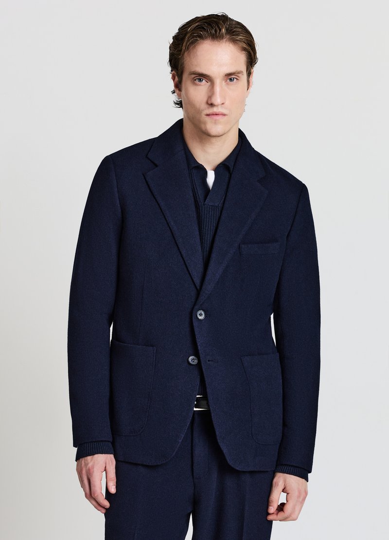 Marineblauer Wollblazer mit kanneliertem Revers, zwei Fronttaschen und einreihiger Knopfleiste. Glatte Textur und maßgeschneiderte Passform.